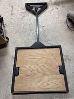 Top view of the square wooden platform with visible grain pattern, attached to a gray metal frame with fixed handle.