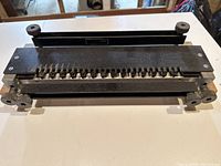 Top view of the metal dovetail router template showing dovetail slots and four adjustable knobs on a light wood base.