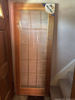 Full view of the wooden door wrapped in plastic with a natural wood finish and multiple clear glass panels.