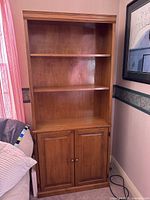 Front view of the wooden bookshelf showing three open shelves and two-door cabinet below.