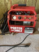 Front view of the Porter-Cable red electric air compressor showing dual outlet fittings, pressure gauge, power cord, and 135 PSI rating.