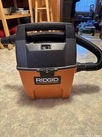 Front view of RIDGID wet/dry vacuum cleaner showing the handle, body, and hose wrapped around.