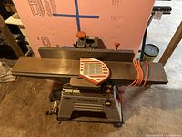 Front view showing cast iron infeed and outfeed tables, control knobs and coiled orange power cord on tabletop