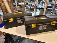 Two closed black and yellow Strong N' Tuff tool boxes on a work table in a workshop.