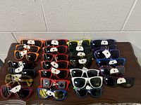 Photo showing 27 pairs of multicolored frame sunglasses with dark lenses arranged on a table in rows and columns.