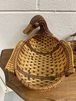 Photo of a vintage wicker basket shaped like a duck with woven body and head, showing natural wicker tones and handwoven craftsmanship.