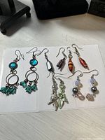 Photo showing all five pairs of dangle earrings arranged on white surface, displaying color and design details
