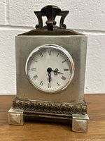 Front view of Canfloyd mantel clock showing white clock face with Roman numerals and ornate black hands within stone-like case with metallic handle