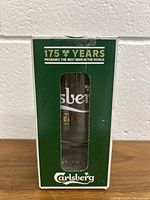 Green box packaging of the 175 years Carlsberg limited edition glass, with a front window showing the glass inside. Text declares 175 years and Carlsberg branding.