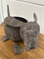 Front and side view of a metal dog-shaped flower planter with detailed ears, face, and feet, showing the hollow body where a plant can be placed.