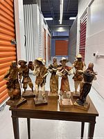 Seven handcrafted paper mache figurines on a wood table in storage unit, diverse Mexican folk art characters with musical instruments and accessories