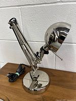 Side angle photo of the chrome modern desk lamp showing adjustable arm, round base, spherical head, and power cord.