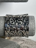 Front view of a wide cuff bracelet made of shiny silver stainless steel with intricate openwork scroll design.