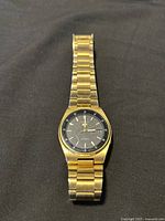 Full view of the Seiko men's wristwatch showing gold metal band and black dial with day-date feature.