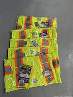 Five Viking brand safety vests packaged in clear plastic, showing bright green color and reflective orange and silver stripes.