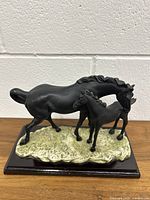 Front view showing the mother horse and baby horse standing closely on a textured base with dark wood platform.
