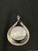Front view of the pendant showing abstract teardrop silver design with circular light inset.