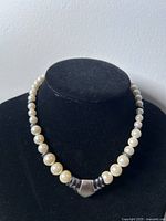 Front view of vintage ivory bead necklace displayed on black necklace stand showing beads and metal clasp detail.