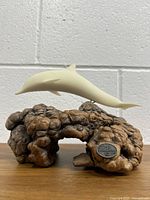 Front view showing the dolphin sculpture mounted over the irregularly shaped burlwood driftwood base with artist plaque visible.