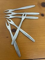 Five vintage stainless steel fruit snack forks laid on a wooden surface showing overall shape and length.