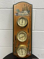 Front view of wooden weather station showing duck illustration and three brass instruments