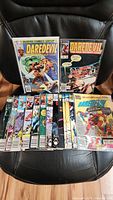 Photo showing all 15 vintage Daredevil comic books arranged on a chair, covers visible with colorful artwork