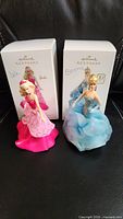 Two Barbie Hallmark Keepsake collectible figures with their original boxes, one in a pink gown and one in a blue gown, displayed on black background.