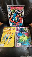 Three vintage Wolverine comic books on black chair surface, titles visible