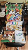 Photo of the four board games stacked; Blokus, The Game of Life 50th Anniversary Edition, Rummoli Deluxe, and Sequence boxed games visible.