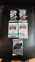 View of all five sealed hockey card packs on black background showing designs and wrappers