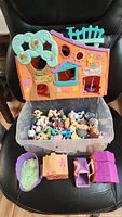 Photo showing plastic orange and blue Littlest Pet Shop playhouse, transparent container with many small Littlest Pet Shop figures inside, and several accessory items placed in front of container.