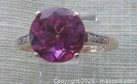 Close-up image of the round faceted amethyst gemstone prong set in the yellow gold ring showing deep purple color and two tiny diamonds on each side.