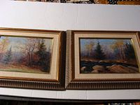 Both framed oil paintings shown side by side on a table with white surface.