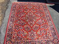 Full view of larger red floral carpet laid on pavement showing overall pattern and condition.