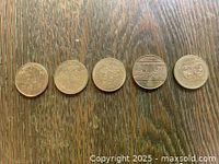 Photo of five circulated Canadian one-dollar commemorative coins showing various side designs