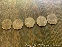 Five Canadian Voyager one-dollar coins laid out on wood surface, showing the reverse side with the Voyageur canoe design.