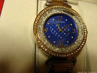 Close-up photo of the watch face showing blue dial with gold numerals and rhinestone bezel
