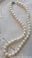 Full view of the cultured freshwater pearl necklace displayed on a lace-trimmed fabric background.