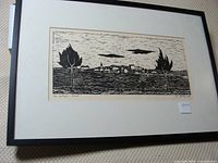 Framed black and white woodcut print showing a rural landscape scene with a village, trees, and sky.