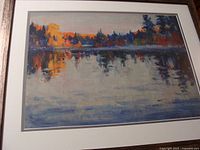 Full view of one framed print showing a lake with trees reflecting autumn colors, signed by Manly MacDonald