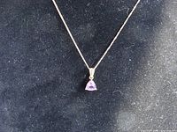 Full view of the necklace with triangular amethyst pendant on black background showing chain length and overall design.
