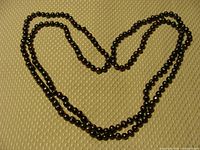 Full view of the necklace arranged on a textured sepia-beige background, showing length and stringing of black pearls.