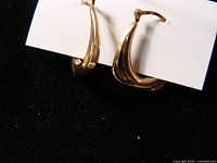Front side view of the two gold earrings showing their curved half-hoop shape and polished gold surface.