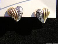 Pair of heart shaped 2-tone gold earrings displayed on a white and black background, showing both earrings with clear texture and shine.