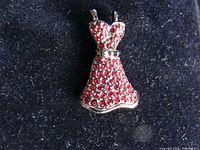 Front view of the brooch showing the dress shape encrusted with red crystals.