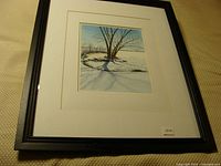 Framed watercolor painting showing winter scene with snow, trees, and shadows.