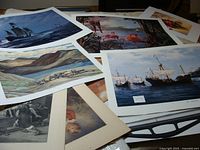 Multiple art prints spread out showing maritime scenes and landscape prints