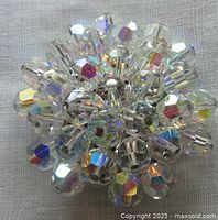 Close-up front view of the circular brooch showing reflective aurora borealis faceted crystal beads densely arranged on a silver-tone metal base.