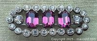 Top view of a vintage brooch showing three emerald-cut purple glass stones surrounded by clear round bezel set stones.