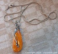 Full view of the amber pendant along with the silver chain laid on fabric background.